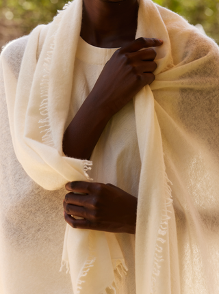 A white open-knitted cashmere shawl wrapped around a woman's shoulders