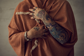 Man with heavily tattooed arms has wrapped himself with a cashmere woven blanket throw in a rust colour by KASMIRI