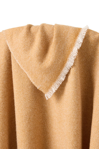 Close-up of a cashmere throw blanket in gold with white trim on a white background