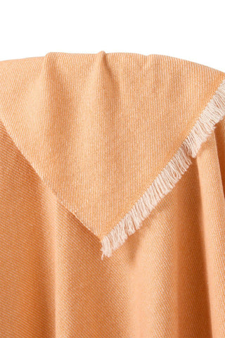 Close-up of a peach-colored cashmere throw blanket with frayed edges on a white background