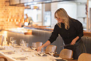 Person setting a table in a restaurant with glasses and cutlery.