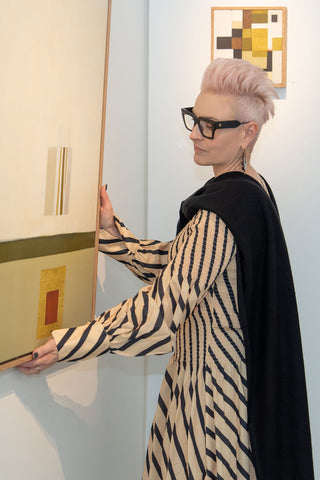 Sophie Vander wears cashmere Black Travel Wrap by Kasmiri in art gallery setting holding a painting by Leonie Barton. 