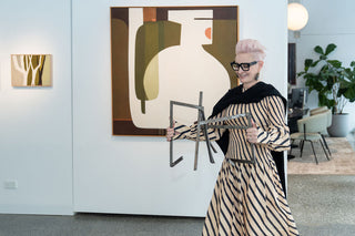 Sophie Vander wears Kasmiri Cashmere Wrap in black while holding a scultpure by Caroline Duffy. Abstract paintings behind her by Leonie Barton. 