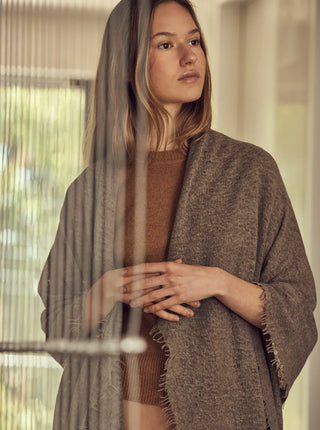 woman wearing an undyed organice cashmere shawl around her shoulders with fringes on either side of the shawl. 
