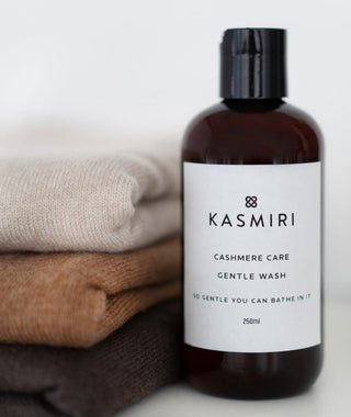 Bottle of Kasmiri Cashmere Care Gentle Wash with folded cashmere garments in the background.