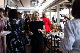 Samantha Theron in a black dress standing in a social setting with other people.