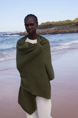Person wrapped in a green blanket on a beach with ocean and sky in the background