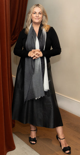women in black wears a Kasmiri ombre grey cashmere scarf. She stands next to a red curtain. 