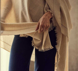 Person wearing a beige cashmere shawl over a dark blue outfit against a neutral background