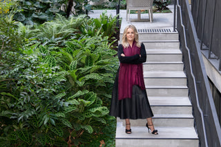 Woman in a black wearing a kasmiri shawl in merlot burgundy  standing on a staircase with greenery on one side.