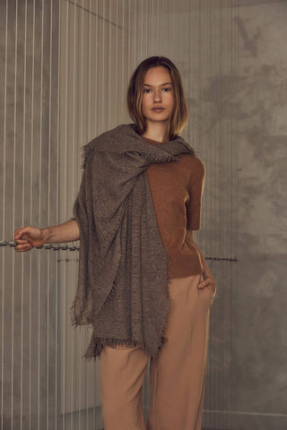 Woman wearing a brown shawl over a brown top and beige pants in a neutral setting