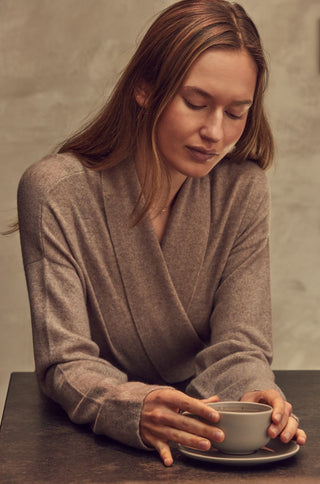 Woman in a neutral coloured cashmere robe holding a cup of coffee against a neutral background