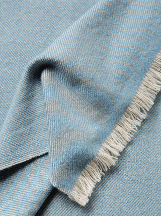cashmere throw blanket in blue with a diagonal weave and white fringes close up