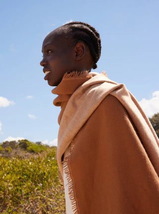 woman has a two toned  neutral cashmere shawl wrapped around her shoulders against a blue clear sky