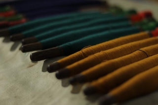 a row of cashmere bobbins in gold and teal ready to be used to weave Kasmiri cashmere scarves